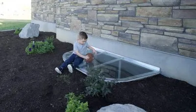 little boy sitting on plastic basement window well cover